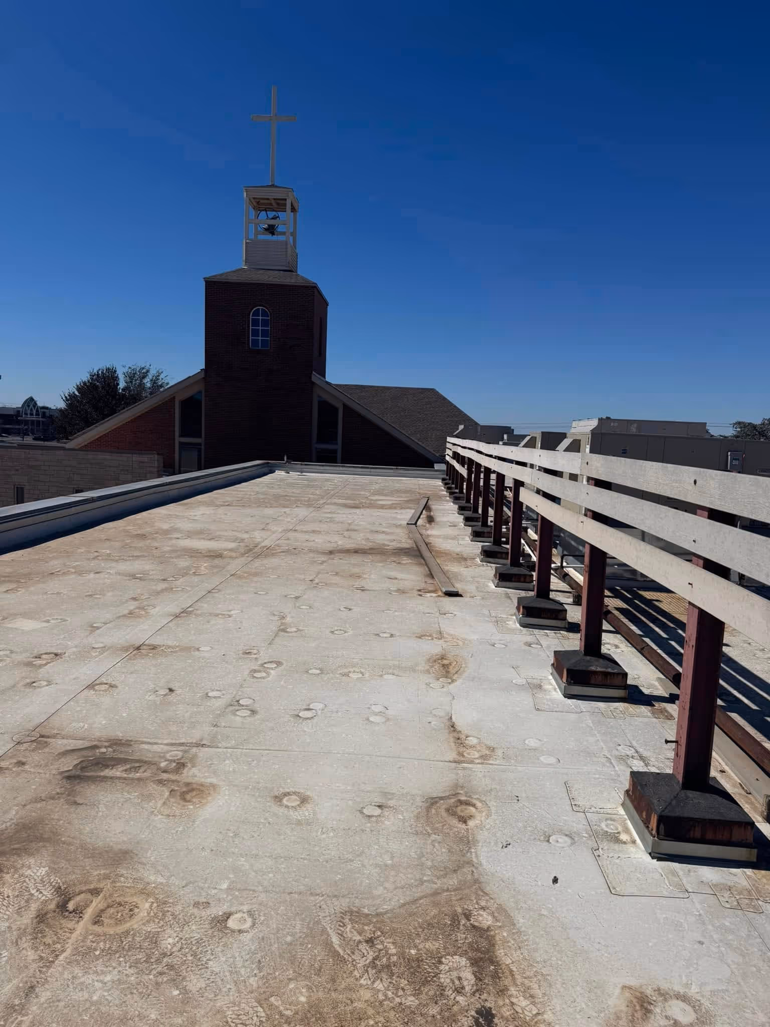 Flat commercial roof with a railing and a church steeple in the background.