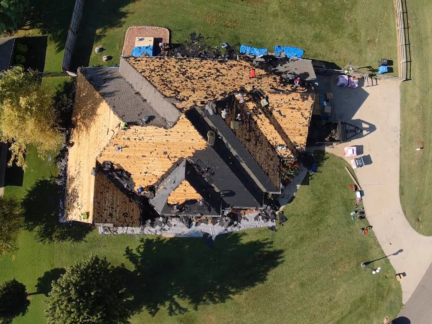 Aerial view of a house mid tear-off with the old roof removed down to the wood decking.