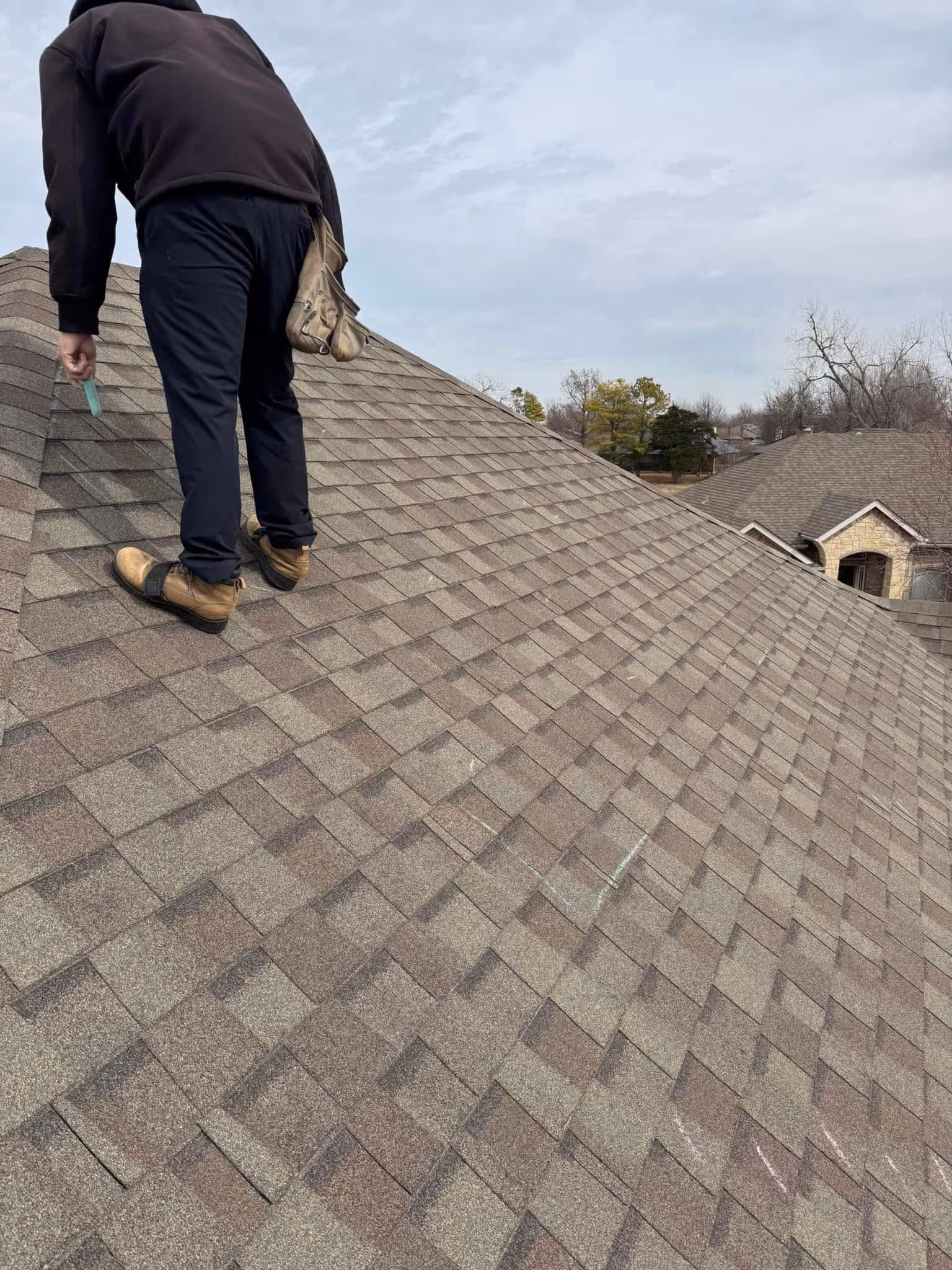 Roofer working on a sloped shingle roof on a clear day.