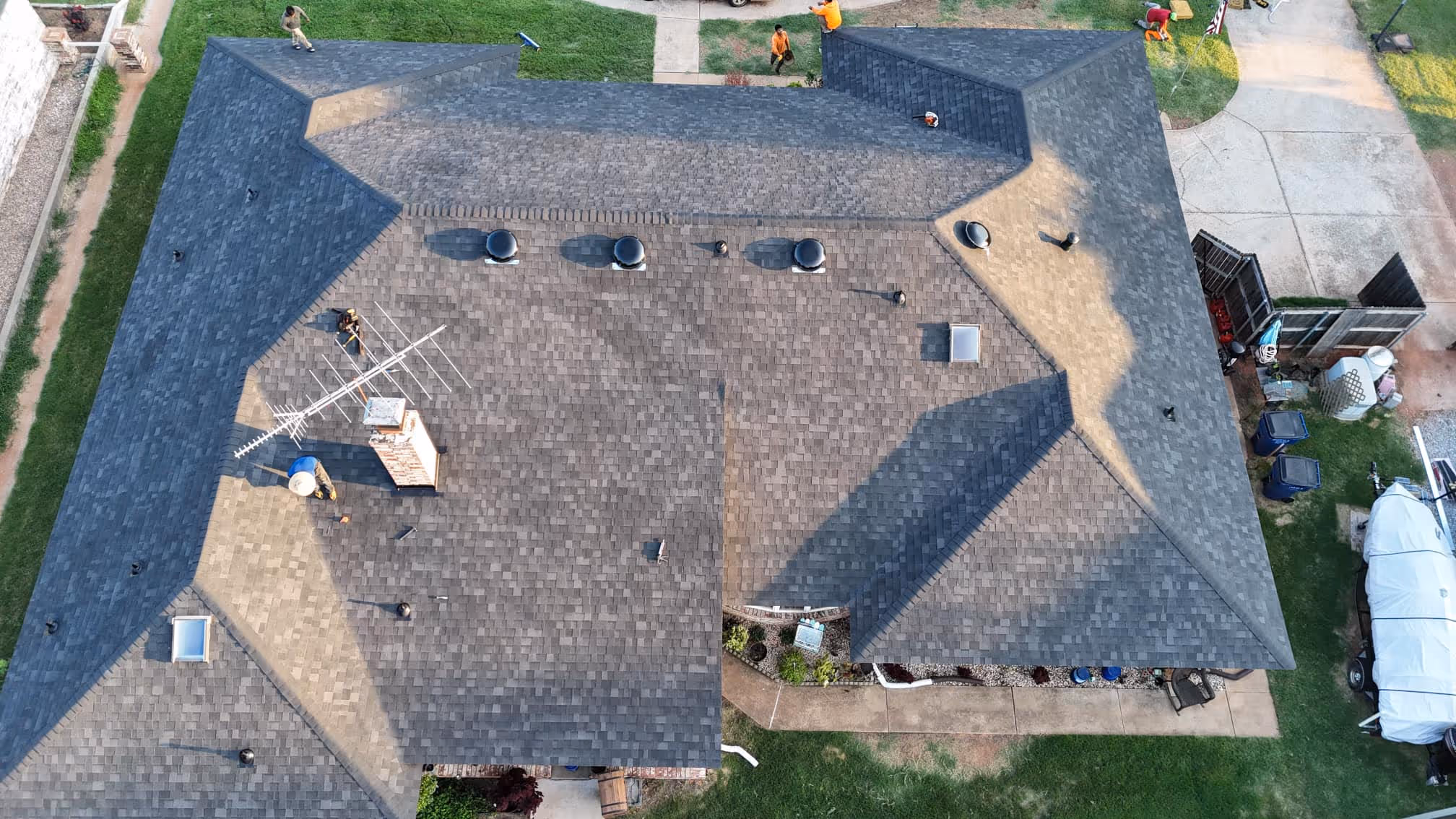 Aerial view of a home with a newly finished dark shingle roof and a green lawn.