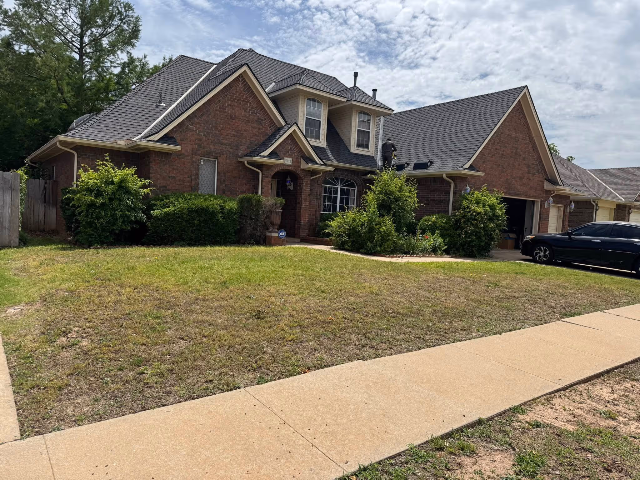 Two-story brick home with a newly installed dark shingle roof and a manicured lawn.