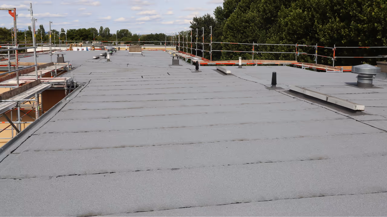 Flat commercial roof with newly installed gray roofing material and safety railings around the perimeter.